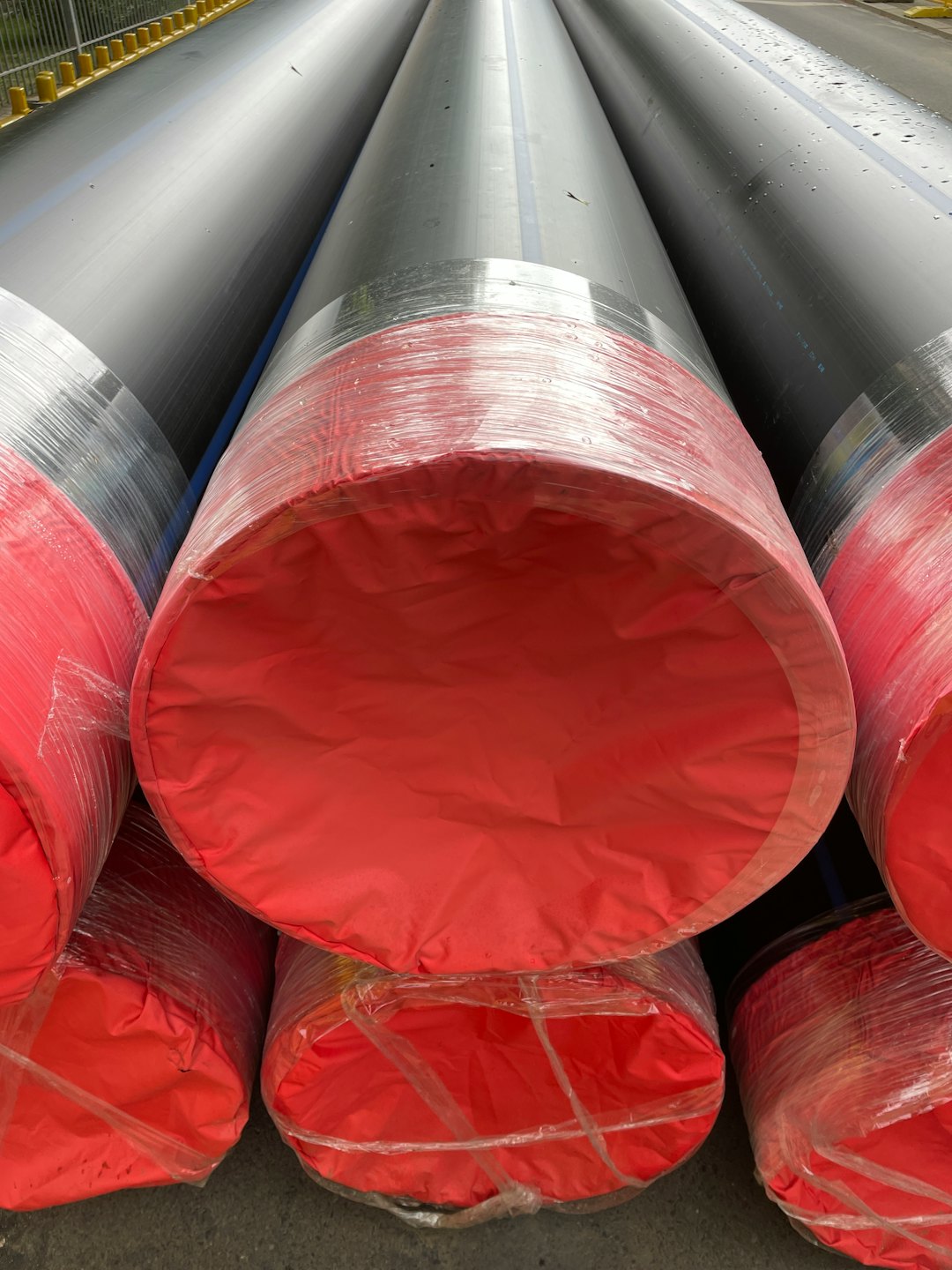 Stacked industrial pipes with red protective fabric covers.